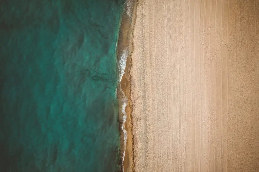 The edge of the sea meeting pale sand, photographed from directly above.