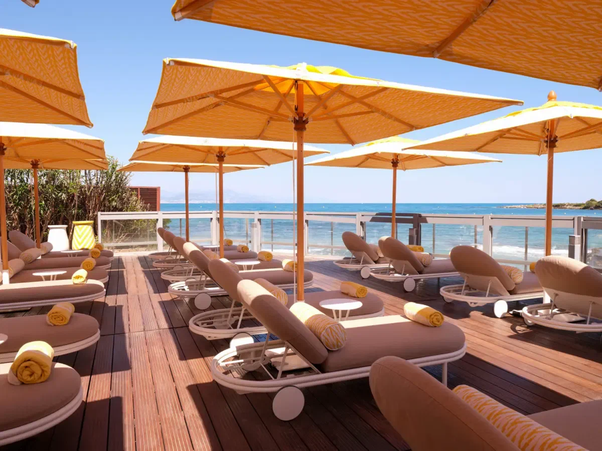 A shaded terrace above the sea, deck shadows falling across the boards and loungers set out beyond.