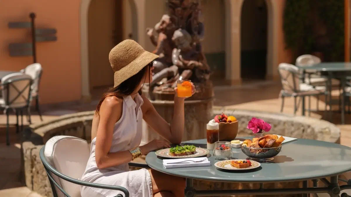 Breakfast at a laid table in a hotel courtyard, a stone fountain and terracotta walls behind.