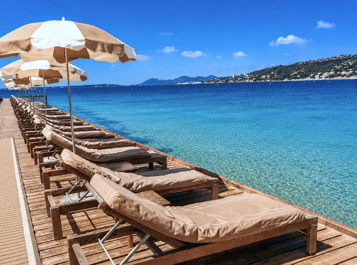 Teak loungers and cream parasols in a long row along a timber pontoon over clear water.
