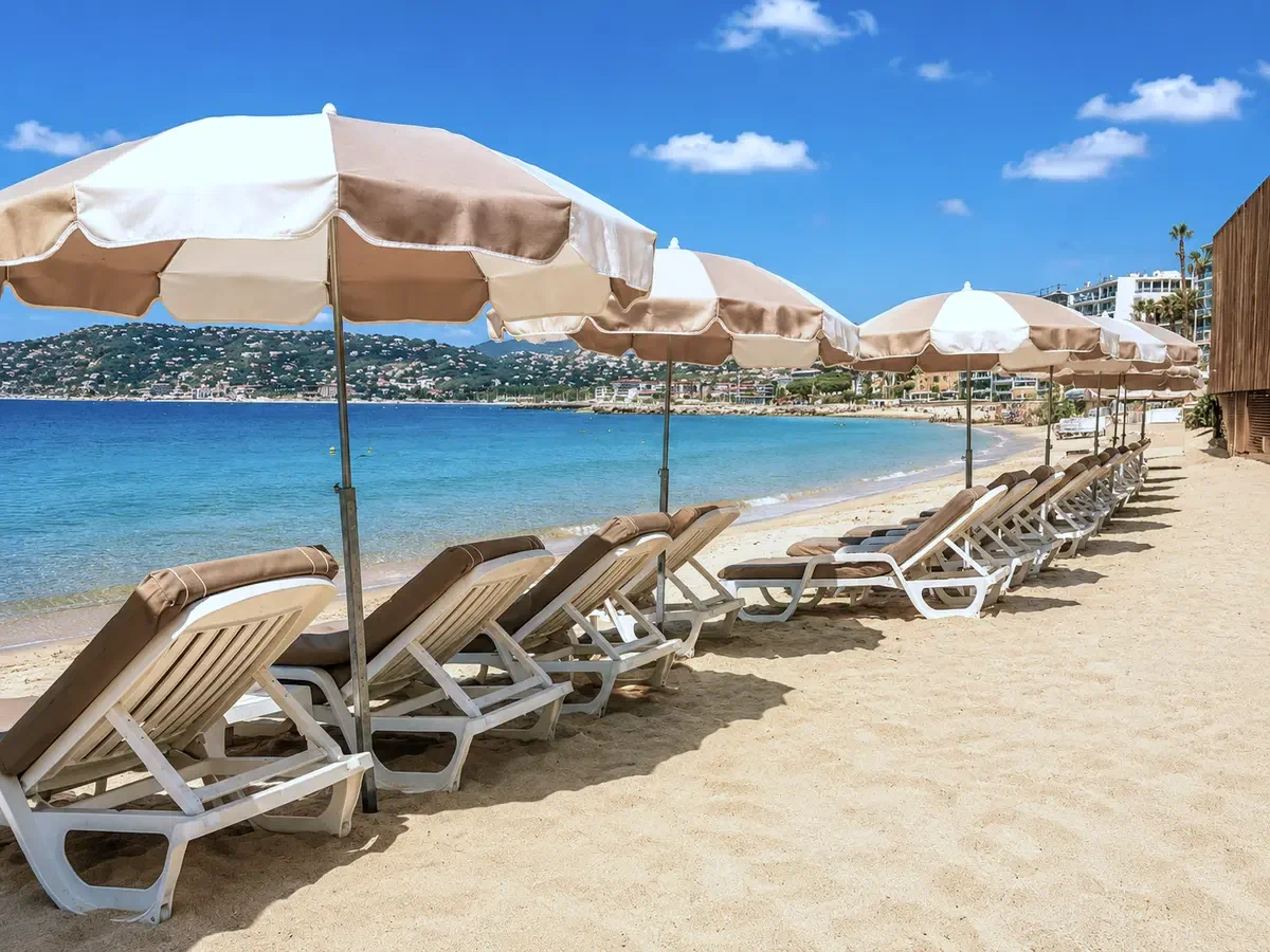 Tan and cream parasols standing over loungers along a curving bay, the water pale green at the shore.