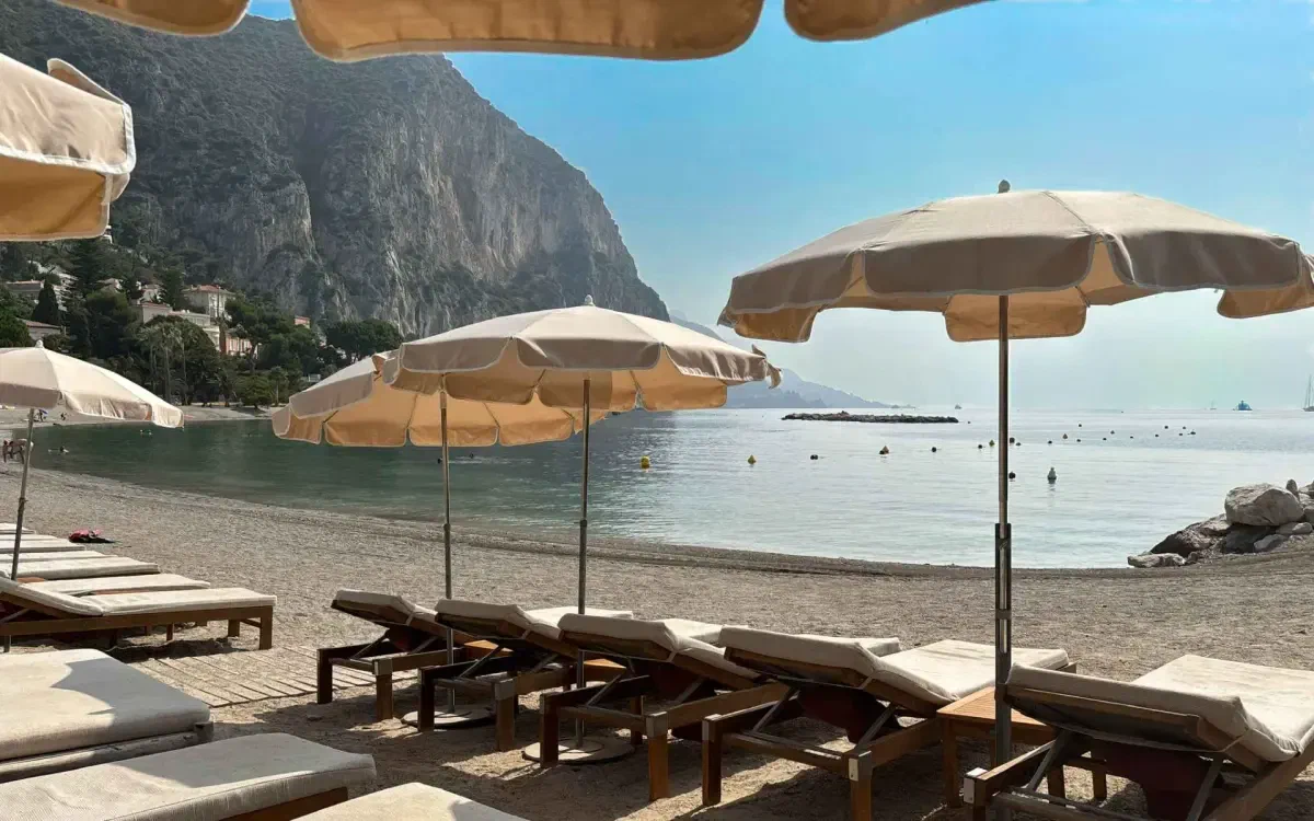 Cream parasols and loungers on a quiet beach, a headland standing over still water in the haze.
