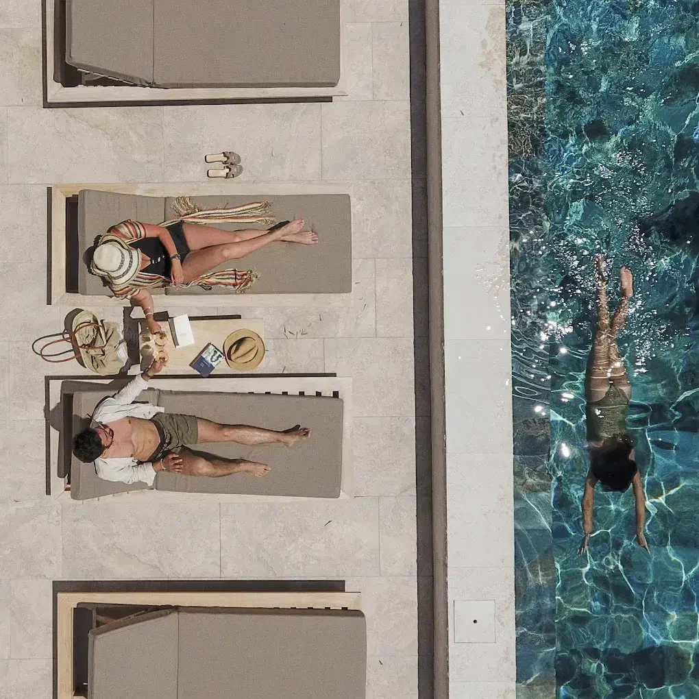 Seen from above, loungers on pale stone beside a pool, a swimmer gliding through the water.